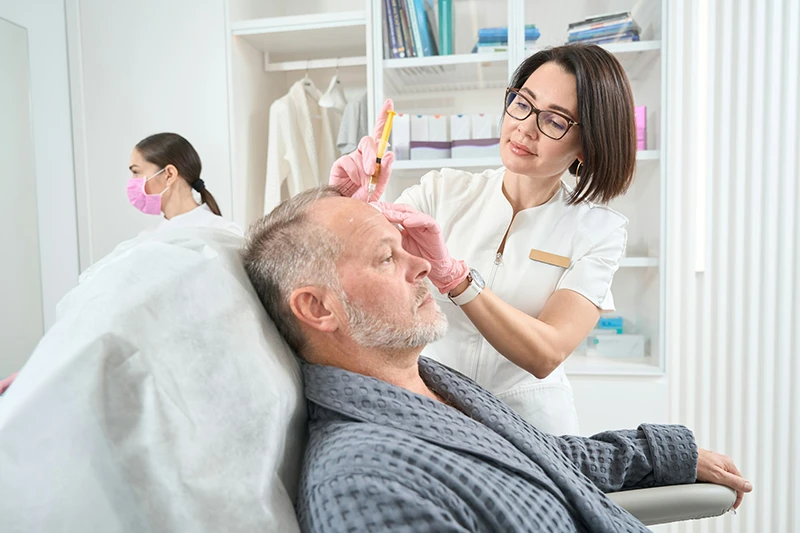 Dermatologist makes injections in the forehead of man with beard