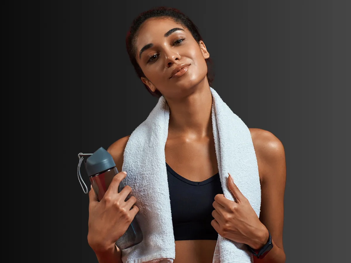 Athletic woman holding a water bottle with a towel around her neck after a workout